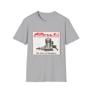 May include: Gray t-shirt featuring a rectangular graphic with the Rossi logo and a detailed illustration of an engine. The text "the choice of champions" is below the engine image.