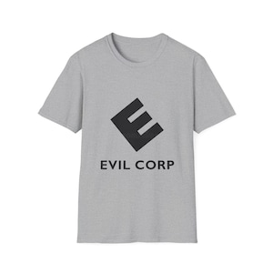 May include: A light gray t-shirt featuring a black, stylized "E" logo within a diamond shape, with the words "EVIL CORP" printed below in black. The shirt has short sleeves and a crew neck.