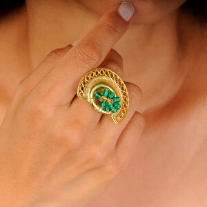 May include: A gold ring with a green stone design. The ring is in the shape of a half-circle and has a delicate filigree pattern.