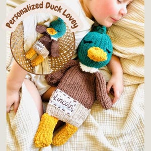 May include: A handmade, personalized duck lovey. The duck has a teal head, yellow beak, and brown body. The name "Lincoln" is stitched on the duck's belly. The text "Personalized Duck Lovey" is in a circular design at the top.
