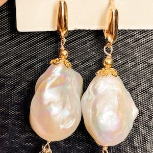 May include: A pair of gold hoop earrings with a large white baroque pearl dangling from each hoop.  Each pearl is accented with a gold filigree design and a cluster of small, colorful gemstones.