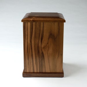 May include: A wooden box with a dark brown finish. The box has a simple, rectangular shape with a slightly raised lid.