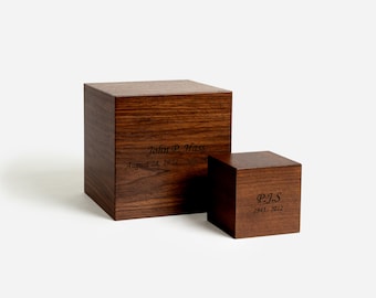May include: Two wooden cremation urns with engraved names and dates. The larger urn is labeled "John P. Hass August 28, 1924 - January 28"