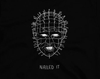 May include: Black t-shirt with a white outline of a character from the movie Hellraiser. The text "NAILED IT" is printed below the character.