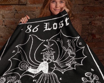 May include: A black and white throw blanket with a graphic design of a figure with wings and the text "86 LOST".
