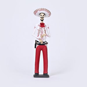 Op de afbeelding: Een wit skeletfiguur dat een rood en wit charro-pak draagt en een grote witte sombrero. Het figuur staat op een zwarte basis.