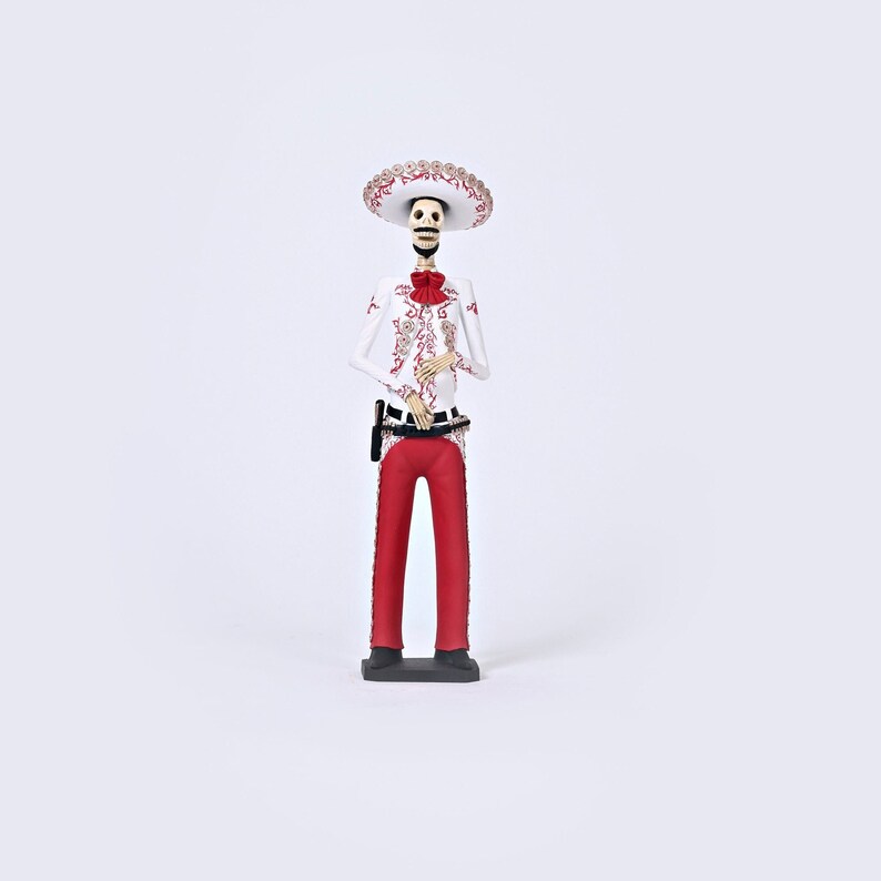 Op de afbeelding: Een wit skeletfiguur dat een rood en wit charro-pak draagt en een grote witte sombrero. Het figuur staat op een zwarte basis.
