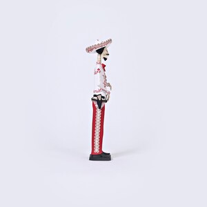 Op de afbeelding: Een wit en rood skeletfiguur met een sombrero en een rood-wit gepatroneerd pak. Het figuur houdt een pistool in zijn rechterhand.