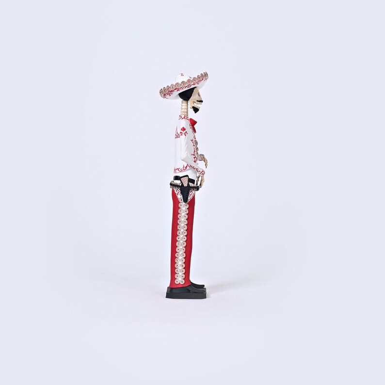 Op de afbeelding: Een wit en rood skeletfiguur met een sombrero en een rood-wit gepatroneerd pak. Het figuur houdt een pistool in zijn rechterhand.