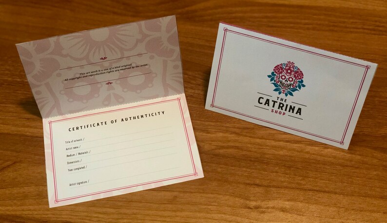 Op de afbeelding: Een echtheidscertificaat met een roze en wit bloemenontwerp. Het certificaat is voor een kunstwerk. De tekst "Echtheidscertificaat" staat in het zwart bovenaan het certificaat. De tekst "Titel van het kunstwerk", "Naam van de kunstenaar", "Medium / Materialen", "Afmetingen", "Jaar van voltooiing" en "Handtekening van de kunstenaar" staat in het zwart onder de titel. Het certificaat is doormidden gevouwen. De achterkant van het certificaat heeft een roze en wit bloemenontwerp. De tekst "Dit kunstwerk is een uniek origineel. Alle auteursrechten en reproductierechten zijn voorbehouden aan de kunstenaar." staat in het zwart onderaan het certificaat.