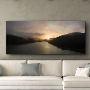 May include: A panoramic photograph of a lake and mountains at sunset, printed on canvas and hung above a white couch in a living room.
