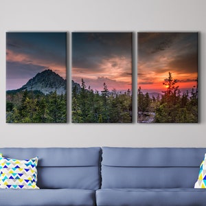 May include: A three-panel canvas print depicting a mountain range with a sunset in the background. The mountain range is covered in trees and the sky is a vibrant orange and pink.