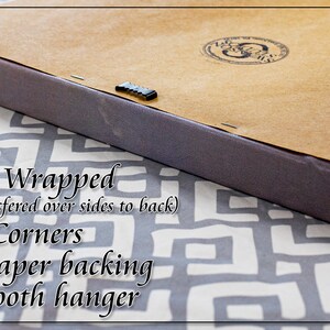 May include: Close-up of the back of a gallery wrapped canvas print. The canvas is wrapped around the edges and secured with staples. The back is covered in brown kraft paper and has a gator tooth hanger.