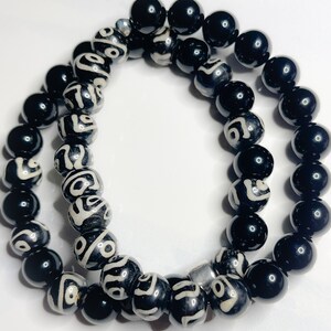 May include: Two black beaded bracelets. One bracelet has black beads with white geometric patterns. The other bracelet has solid black beads.