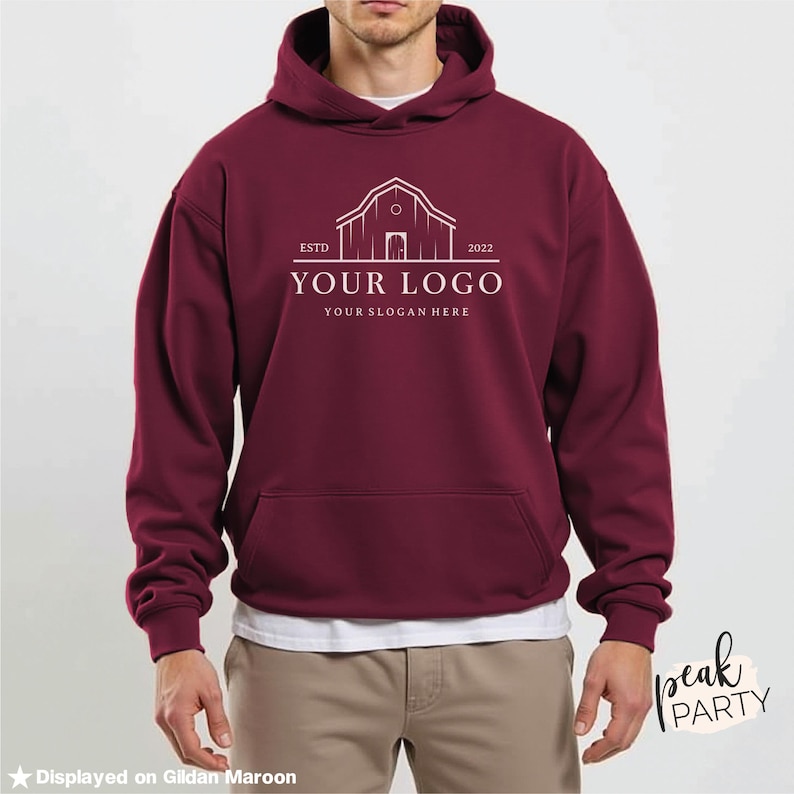 May include: Maroon hoodie with a front pocket and a drawstring hood. The front of the hoodie features a white logo with the text "YOUR LOGO" and "YOUR SLOGAN HERE" below a barn illustration. The text "ESTD 2022" is also included.
