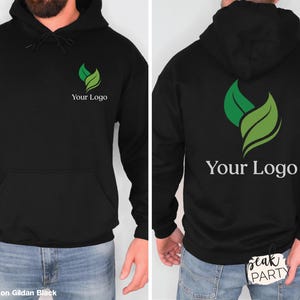 May include: Black hoodie with a front pocket and drawstring hood. The front and back of the hoodie feature a green and white leaf logo with the text "Your Logo" below it. The hoodie is displayed on a person.