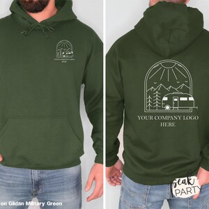 May include: Dark green hoodie with a front pocket and drawstring. The front features a white graphic of a house inside an arch. The back has a white graphic of a camper, mountains, and sun. Text reads "YOUR COMPANY LOGO HERE."