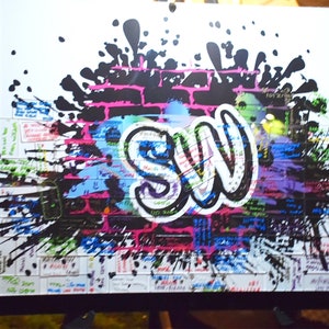 May include: A white canvas with a black brick wall design and a large graffiti-style "SW" in white. The canvas is covered in colorful paint splatters and has a black frame.