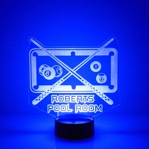 May include: A white acrylic night light shaped like a pool table with crossed pool cues and billiard balls. The light has the text "ROBERTS POOL ROOM" on the bottom.