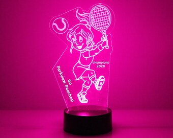 Op de afbeelding: Een wit acryl nachtlampje met een cartoonmeisje dat tennis speelt. Het lampje heeft de tekst "Parkview Go Peaches!" en "champions 2020" erop.