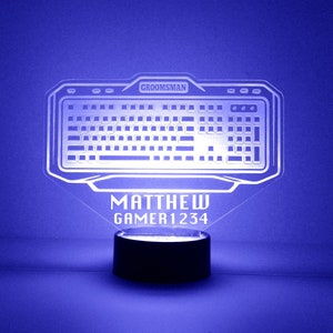 May include: A white acrylic night light shaped like a computer keyboard with the text "GROOMSMAN" at the top and "MATTHEW GAMER1234" at the bottom. The light is on a black base.