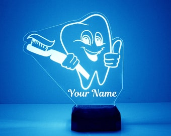 May include: A white acrylic night light shaped like a smiling tooth holding a toothbrush. The light has a black base and says "Your Name" on the front.