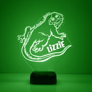 May include: A white iguana silhouette night light with a black base. The iguana is facing right and has a curled tail. The name "Lizzie" is written below the iguana.
