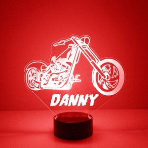 May include: White silhouette of a motorcycle with the name "DANNY" underneath. The motorcycle is on a black base with a red background.