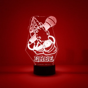 May include: White acrylic night light with a design of two hands holding a microphone and the word "RARE" underneath. The night light is on a black base.
