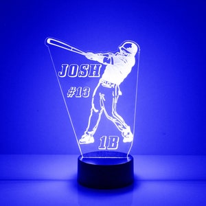 May include: White acrylic night light with a baseball player silhouette, the name "Josh" and the number "#13" and "1B" on the base. The light is on a black base.