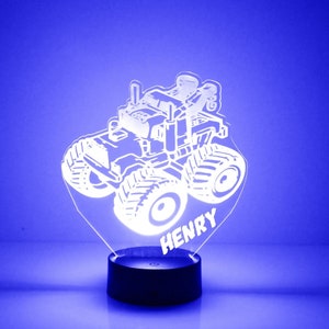 Puede incluir: Una silueta blanca de un camión monstruo con el nombre "HENRY" debajo. El camión está sobre una base negra con una luz azul que brilla a través del acrílico.