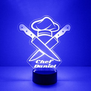 May include: White LED night light featuring a chef's hat and crossed knives design. The light has a black base and the text "Chef Daniel" is inscribed on the front.