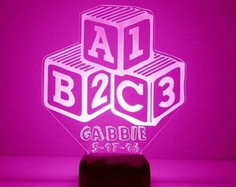 May include: A pink night light shaped like a stack of blocks with the letters A, B, and C and the numbers 1, 2, and 3. The name "Gabbie" and the date "5-17-16" are written below the blocks.