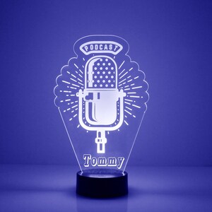 May include: A white acrylic night light shaped like a microphone with the word "PODCAST" above it and the name "Tommy" below it. The light is on a black base.