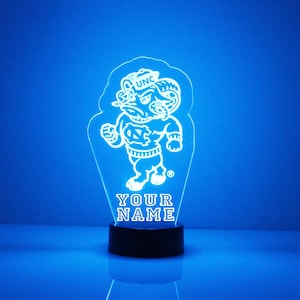Pu&ograve; includere: Una luce notturna in acrilico bianco stampata in 3D con la mascotte dei Tar Heels della Carolina del Nord, Rameses, che indossa un cappello con la scritta "UNC". La luce &egrave; su una base nera e ha le parole "YOUR NAME" stampate sotto la mascotte.