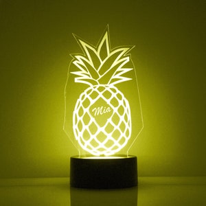 May include: A white pineapple-shaped night light with the name "Mia" in the center. The light is on and illuminating the pineapple shape.