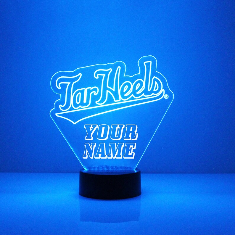 Pu&ograve; includere: Una luce notturna LED blu con un contorno bianco della parola "Tar Heels" e le parole "YOUR NAME" sotto. La luce &egrave; su una base nera.