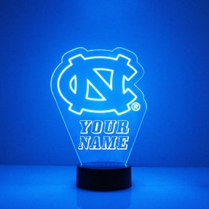 Pu&ograve; includere: Una luce notturna LED blu con un contorno bianco del logo dei Tar Heels dell'Universit&agrave; della Carolina del Nord e il testo "YOUR NAME".