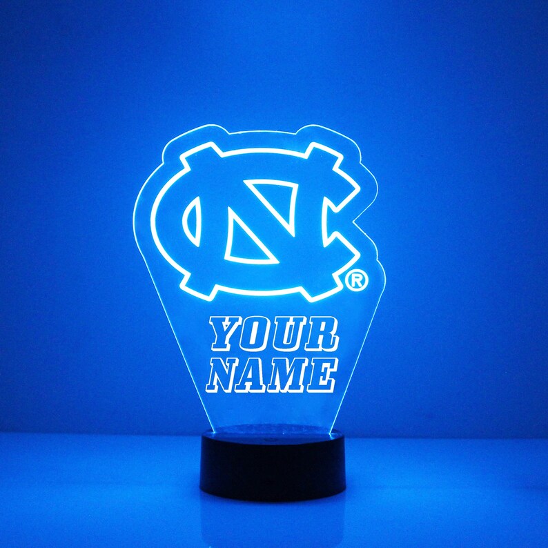 Pu&ograve; includere: Una luce notturna LED blu con un contorno bianco del logo dei Tar Heels dell'Universit&agrave; della Carolina del Nord e il testo "YOUR NAME".