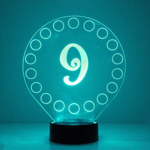 May include: A teal blue night light shaped like a teardrop with a white number 9 in the center. The number is surrounded by a circle of small circles.