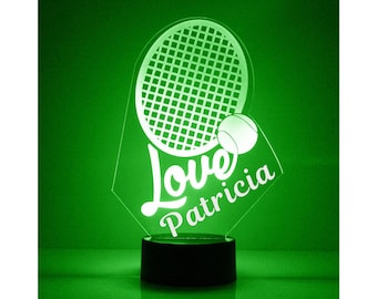Op de afbeelding: Een groen verlicht nachtlampje met een wit tennisracket- en balontwerp. De woorden "Love Patricia" staan onder het racket.