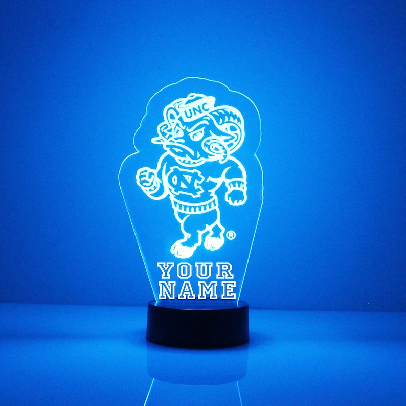Pu&ograve; includere: Una luce notturna in acrilico bianco stampata in 3D con la mascotte dei Tar Heels della Carolina del Nord, Rameses, che indossa un cappello con la scritta "UNC". La luce &egrave; su una base nera e ha le parole "YOUR NAME" stampate sotto la mascotte.