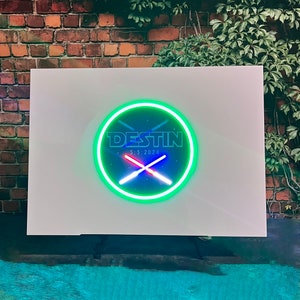 Op de afbeelding: Een wit bord met een groene neoncirkel met de tekst "DESTIN 5.5.2024" en twee gekruiste rode en blauwe lampen.