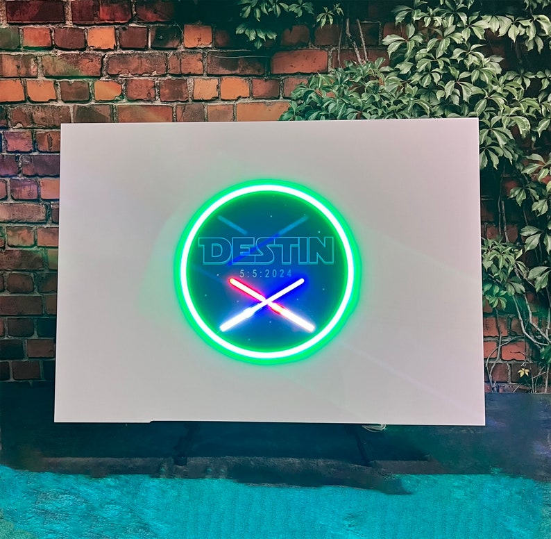Op de afbeelding: Een wit bord met een groene neoncirkel met de tekst "DESTIN 5.5.2024" en twee gekruiste rode en blauwe lampen.