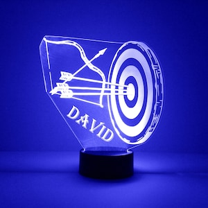 May include: A white acrylic night light with a target and arrows design. The name "DAVID" is engraved on the base.