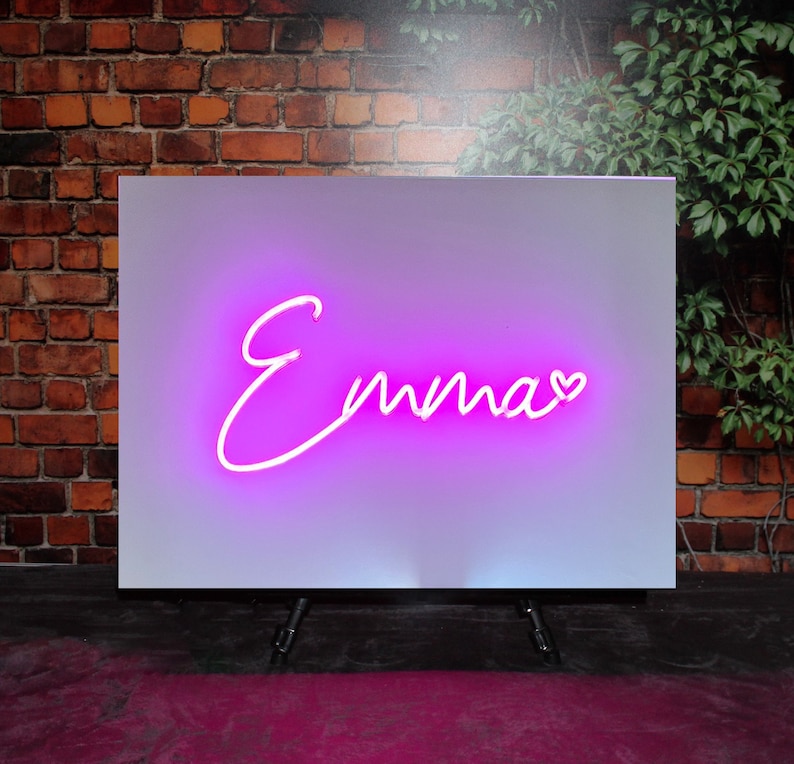Op de afbeelding: Een wit bord met een roze neon-bord met de tekst "Emma" met een klein hartje na de naam.