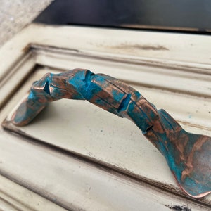 May include: A rustic, hand-forged drawer pull with a distressed copper finish and turquoise accents. The pull has a unique, organic shape and is perfect for adding a touch of farmhouse charm to any home.