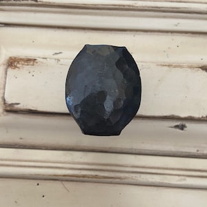 May include: A black hammered metal cabinet knob with an oval shape.