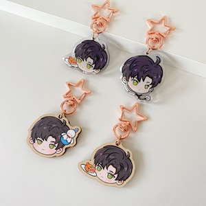May include: Four keychains featuring a cartoon character with dark purple hair and green eyes. Two are clear acrylic and two are wood, all attached to rose gold star-shaped clasps. The character is depicted in various poses, including holding a slice of cake, wearing a stethoscope, or accompanied by a small snowman figure.