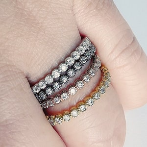May include: Three stacking rings with a bezel setting of small round clear stones. The rings are gold, silver, and black.